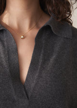 Woman wearing a dark grey polo neck collared jumper and denim wide leg jeans against a beige background