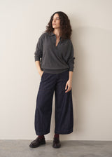 Woman wearing a dark grey polo neck collared jumper and denim wide leg jeans against a beige background