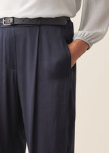 A woman wearing dark blue satin trousers with a pale grey blouse and a dark grey blazer