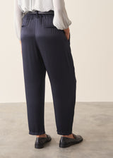 A woman wearing dark blue satin trousers with a pale grey blouse and a dark grey blazer