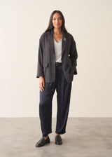 A woman wearing dark blue satin trousers with a pale grey blouse and a dark grey blazer