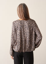 A woman wearing a satin leopard print blouse with a bubble hem and black trousers.