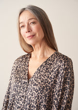 A woman wearing a satin leopard print blouse with a bubble hem and black trousers.