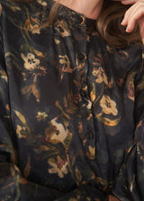 A woman wearing a dark floral satin midi dress with waist tie and button up detail and black chunky boots