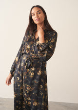 A woman wearing a long-sleeve, dark floral midi dress with a tie waist, set against a plain off-white studio background.
