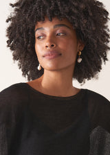 Model wearing gold drop earrings with pearl pendant, styled with a black sweater