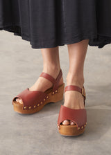 Brown open-toe clogs with wooden soles worn by a person in a black skirt.