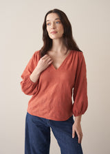 Woman wearing a terracotta cotton blouse with embroidered detail and blue jeans