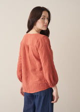 Woman wearing a terracotta cotton blouse with embroidered detail and blue jeans