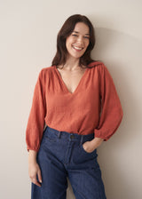 Woman wearing a terracotta cotton blouse with embroidered detail and blue jeans