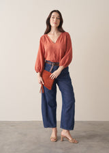 Woman wearing a terracotta cotton blouse with embroidered detail and blue jeans