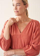 Woman wearing a pale terracotta cotton top with embroidery detail and a light linen skirt