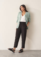 Woman wearing a white embroidered cotton blouse with a V-neck and black trousers against a plain background