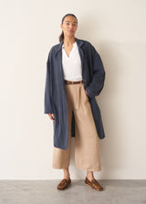 Woman wearing navy trench coat with light trousers and a white top