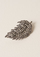 Leaf brooch embellished with smoky-grey crystals, against a beige background