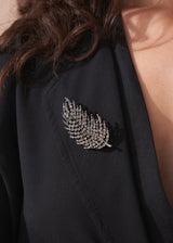 Model wearing a black blazer with a leaf brooch embellished with smoky-grey crystals, against a beige background