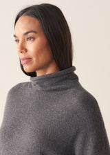 Woman wearing a dark grey high neck sweater with checked trousers against a plain background.