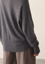 Woman wearing a dark grey high neck sweater with checked trousers against a plain background.
