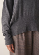Woman wearing a dark grey high neck sweater with checked trousers against a plain background.