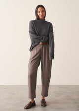 Woman wearing a dark grey high neck sweater with checked trousers against a plain background.