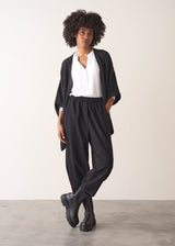 Woman wearing a dark gray cardigan over a white shirt and black trousers against a plain background