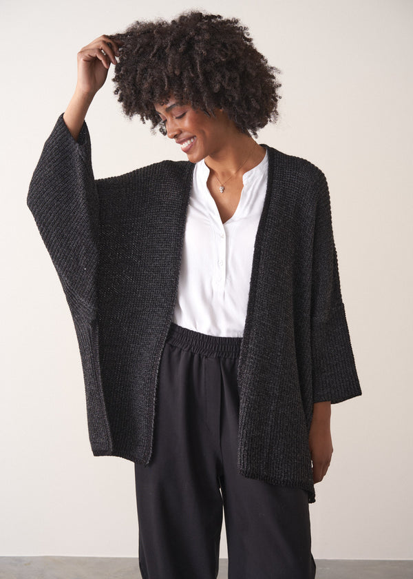 Woman wearing a dark gray cardigan over a white shirt and black trousers against a plain background