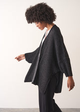 Woman wearing a dark gray cardigan over a white shirt and black trousers against a plain background