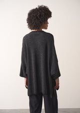 Woman wearing a dark gray cardigan over a white shirt and black trousers against a plain background