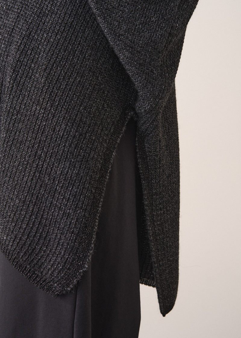 Woman wearing a dark gray cardigan over a white shirt and black trousers against a plain background