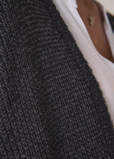 Woman wearing a dark gray cardigan over a white shirt and black trousers against a plain background