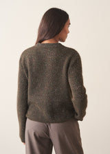 A woman wearing a dark khaki green sequin sweater with brown checked trousers and a black belt
