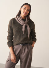 A woman wearing a dark khaki green sequin sweater with brown checked trousers and a black belt