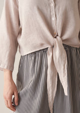 Woman wearing nude tie-front linen shirt with striped wide leg trousers.