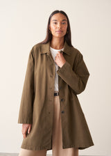 A woman wearing a mid-length khaki green utility trench coat over a white top and beige trousers.