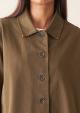 A woman wearing a mid-length khaki green utility trench coat over a white top and beige trousers.