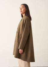 A woman wearing a mid-length khaki green utility trench coat over a white top and beige trousers.