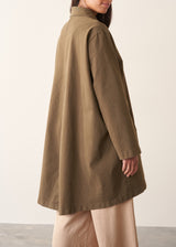 A woman wearing a mid-length khaki green utility trench coat over a white top and beige trousers.