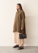 A woman wearing a mid-length khaki green utility trench coat over a white top and beige trousers.