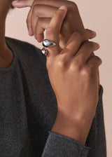 Close-up of a person's hand wearing a chunky silver ring with a beige background
