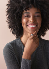 Woman wearing a dark grey shirt with chunky silver ring against a beige background