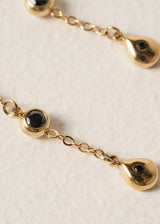 Close up of black crystals on a pair of gold chain drop earrings, set against a beige background