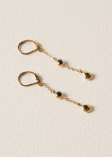 Pair of delicate gold chain drop earrings featuring black crystals, set against a beige background