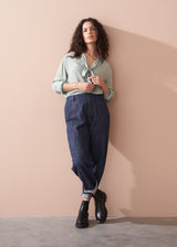Woman wearing a light green blouse and dark blue jeans against a beige wall.