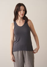 Woman wearing a dark grey tank top and checked linen trousers against a plain background