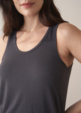 Woman wearing a dark grey tank top and checked linen trousers against a plain background