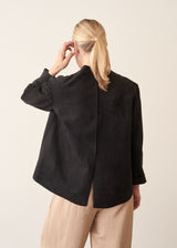 Woman wearing black faux suede boxy jacket and beige cropped trousers