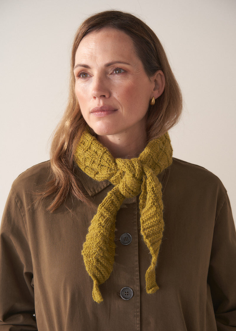 Woman looking into the distance wearing an olive kitted neckscarf with a brown jacket