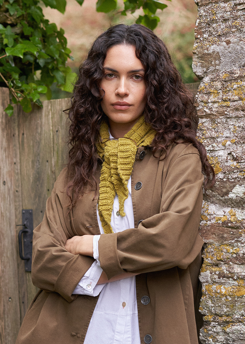 Woman wearing a olive knitted neck scarf with brown trench coat and white blouse