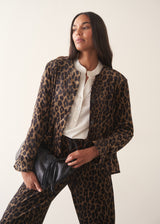 A woman wearing a matching leopard-print jacket and trousers set with a white shirt and a black clutch bag.