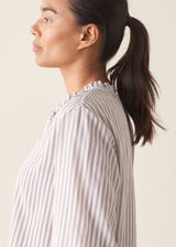Woman wearing white and blue stripe light shirt with ruffle collar and red linen shorts